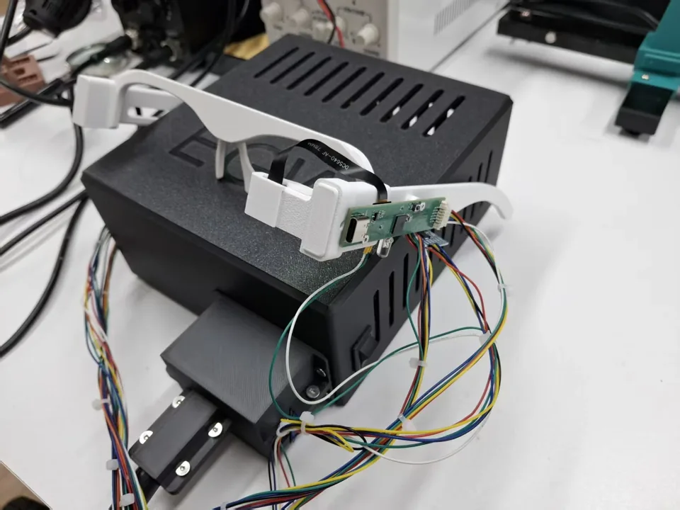 Glasses prototype connected by wires to an electronics enclosure on a workbench